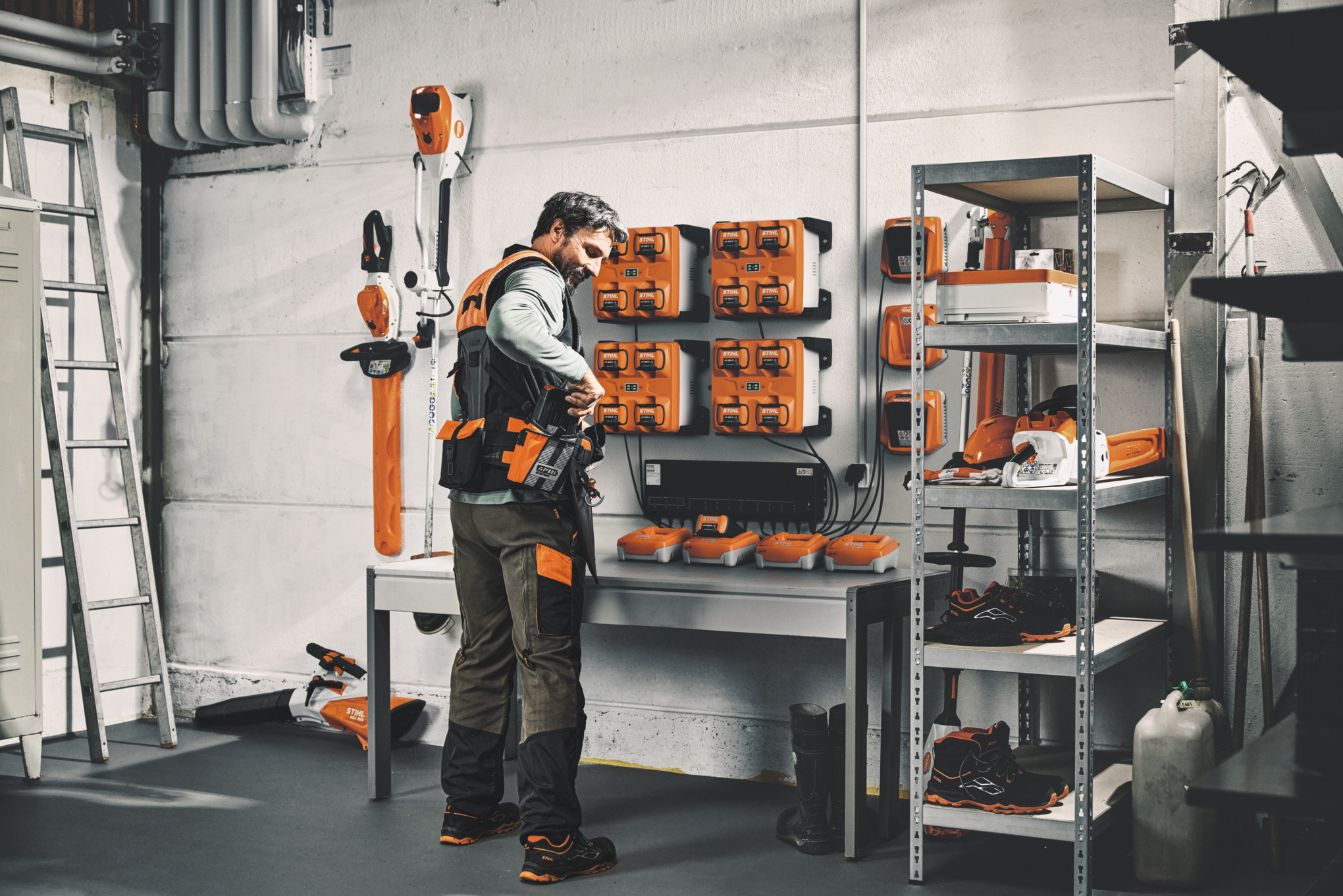 Un hombre en un almacén con herramientas y baterías STIHL lleva el sistema de arnés modular STIHL ADVANCE X-Flex 