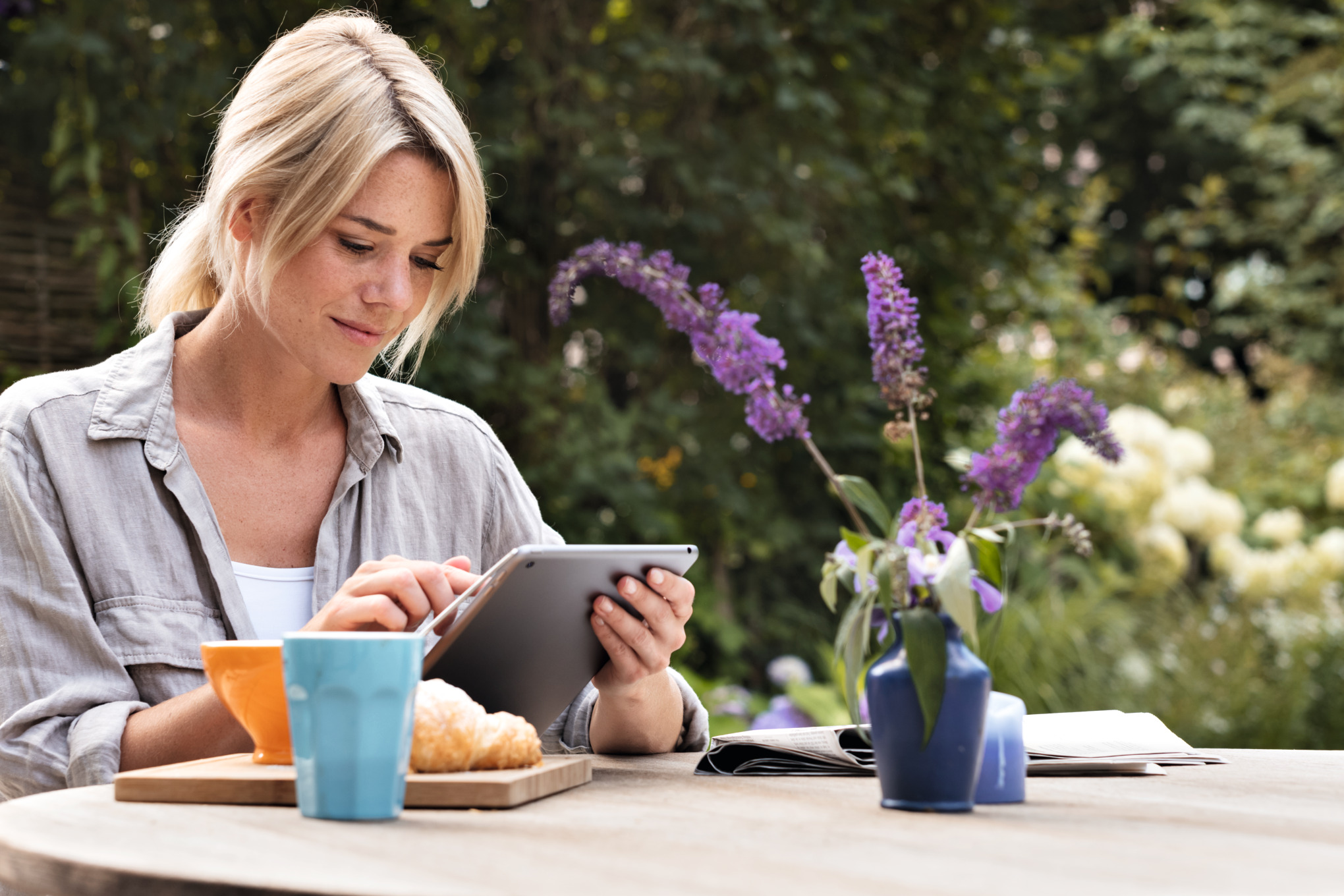 Una mujer utiliza una tableta en la mesa del desayuno en el jardín