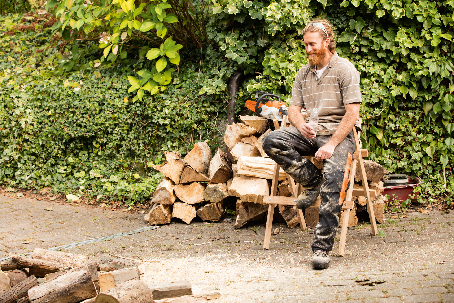 Un hombre está sentado en un caballete de sierra delante de un tronco.