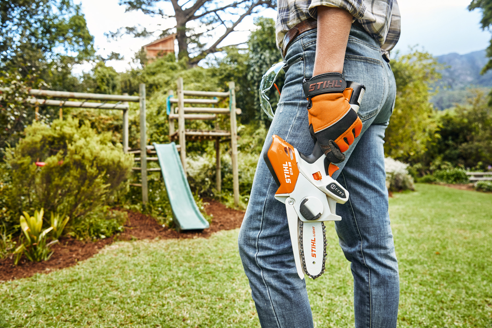 Una persona con una herramienta de poda de batería STIHL GTA 26 delante de un tobogán en el jardín