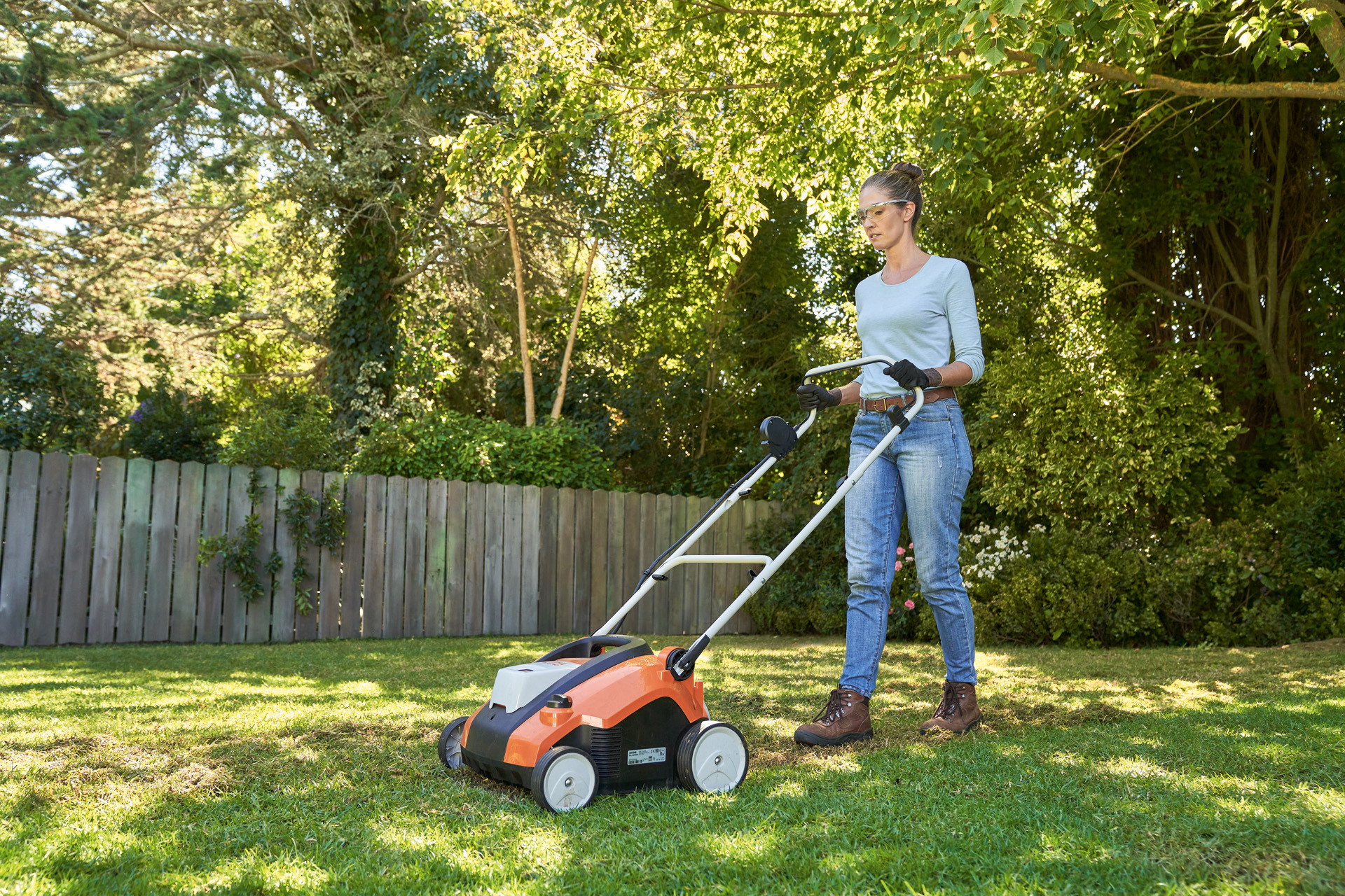 Una mujer airea el césped con el escarificador de batería STIHL RLA 240, equipada con gafas y guantes de trabajo.