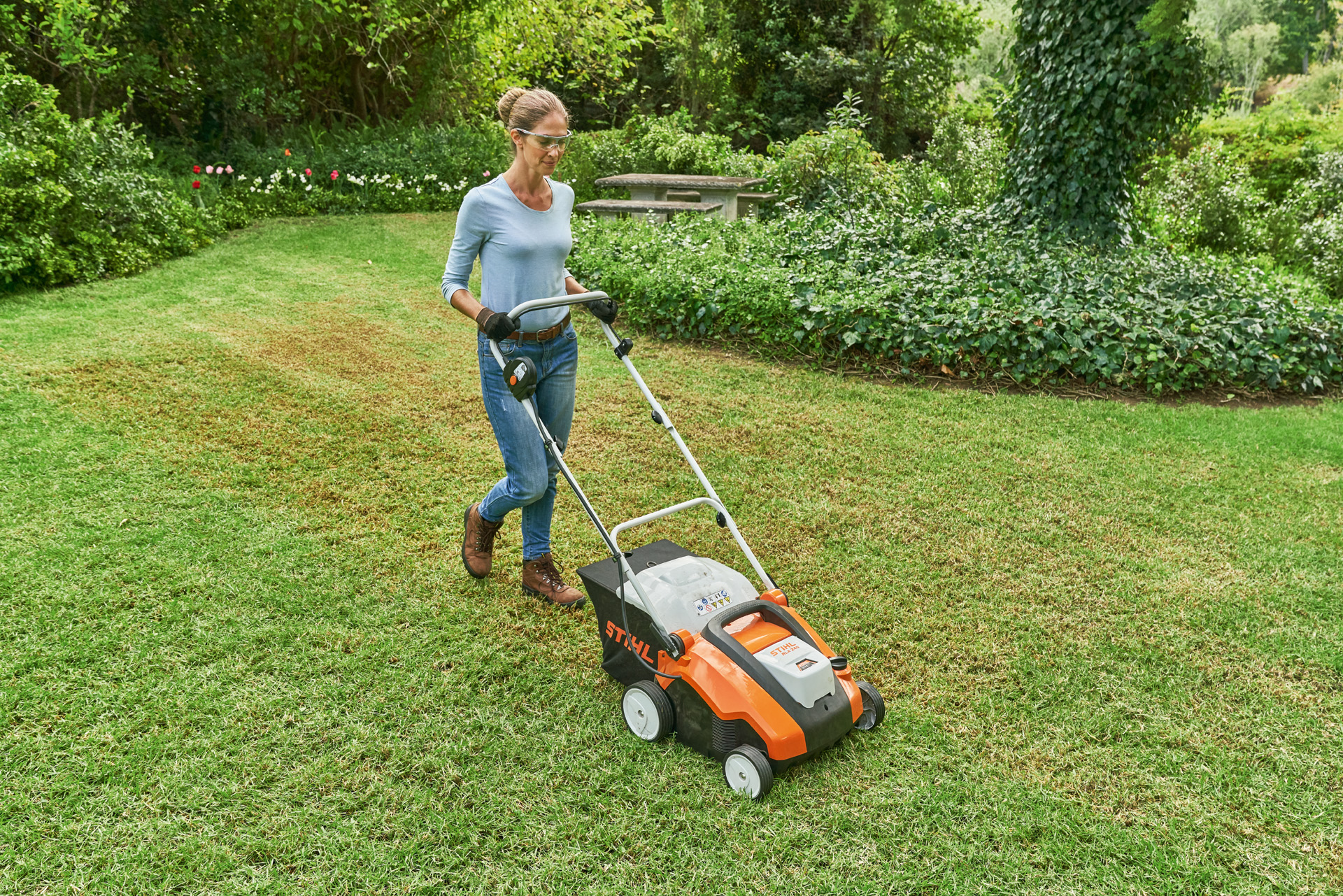 Una mujer con gafas protectoras y guantes escarifica el césped con el escarificador de batería STIHL RLA 240.