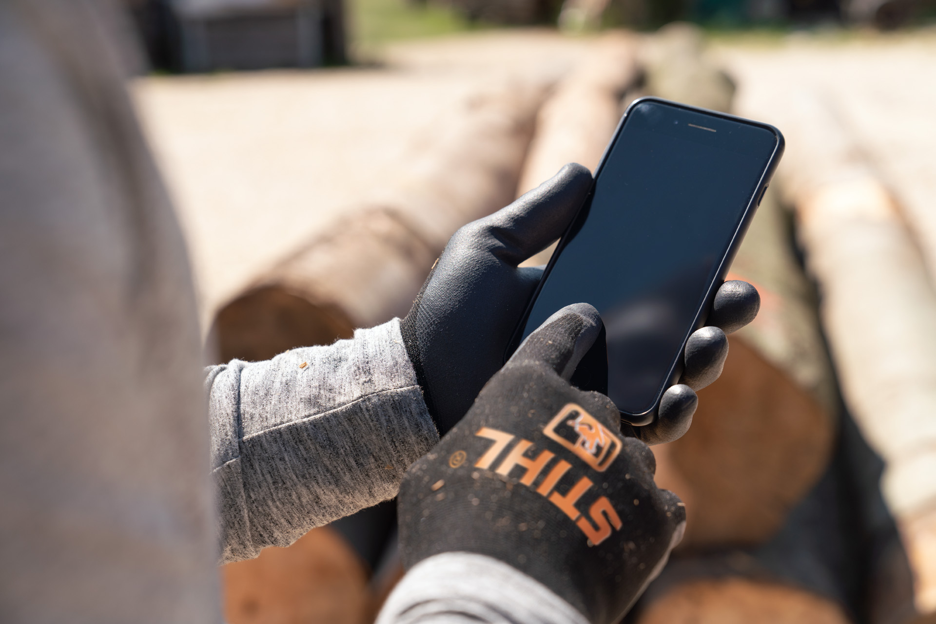 Un hombre con guantes de protección STIHL utiliza su smartphone